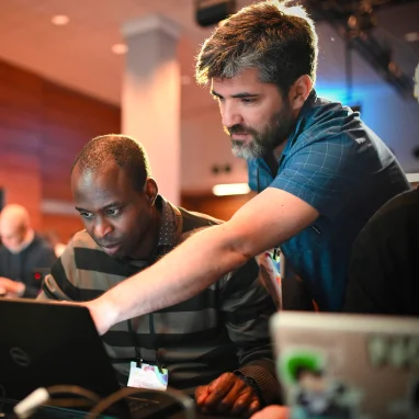 Man leaning over another man's shoulder to show direction on a computer screen