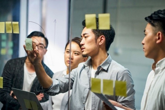 Four people, collaborating  with post its and markers in a room.