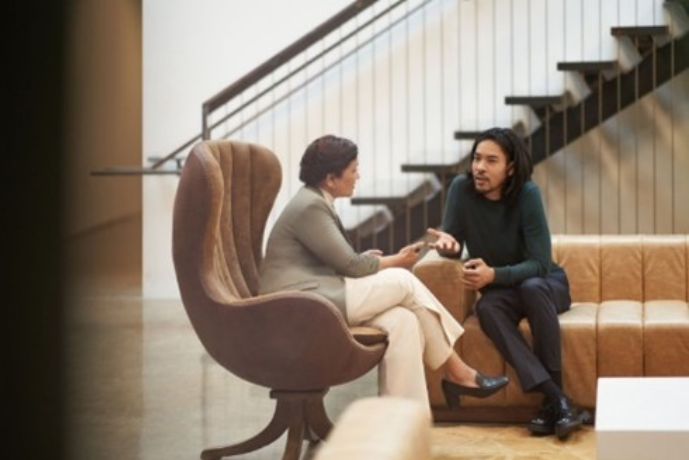 Two people, collaborating in an open space, with couches and stairs in the background.